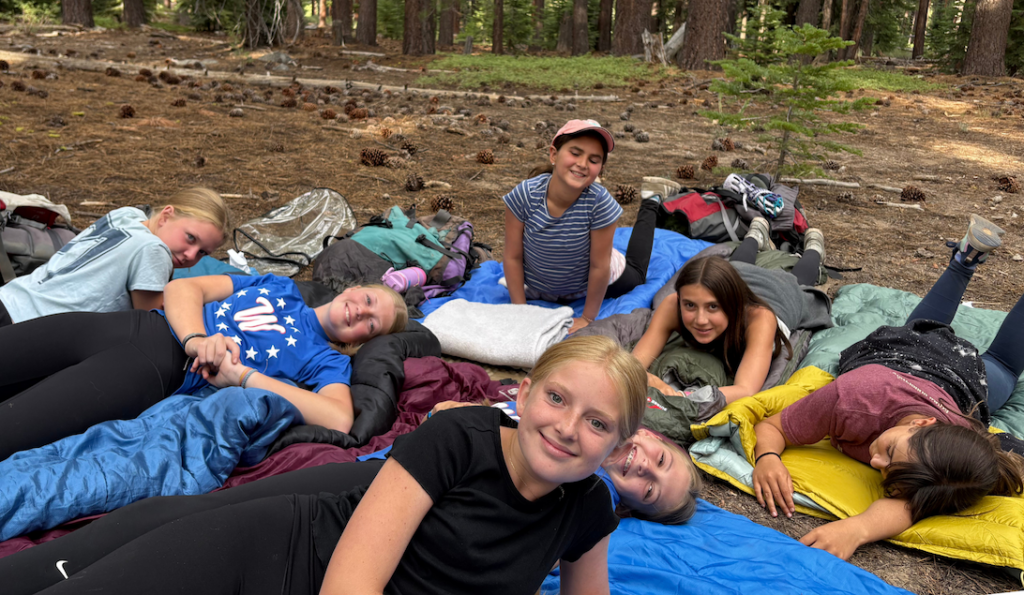 Female campers laying on their sleeping bags during overnight at Galilee Point