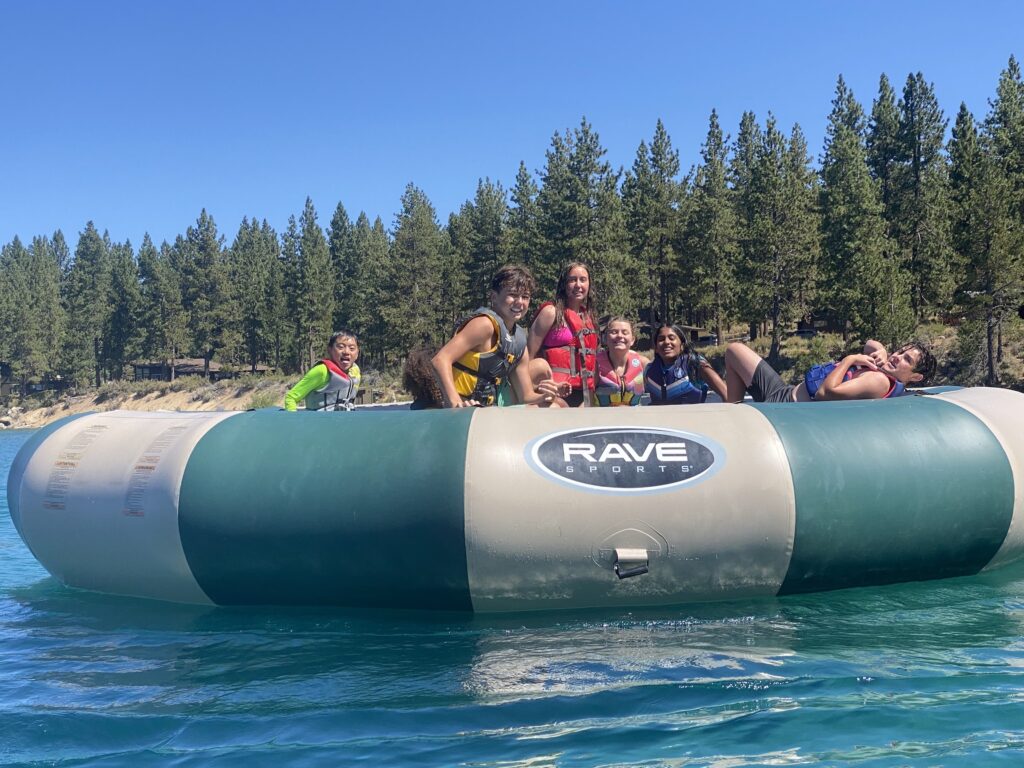 Campers on the water trampoline in Lake Tahoe at Camp Galilee with a view of camp.